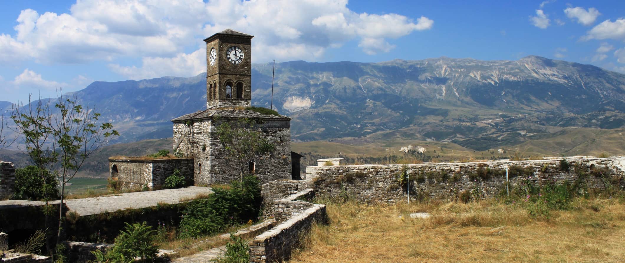 An old stone tower and stone wall in Albania with rolling hills and mountains in the distance