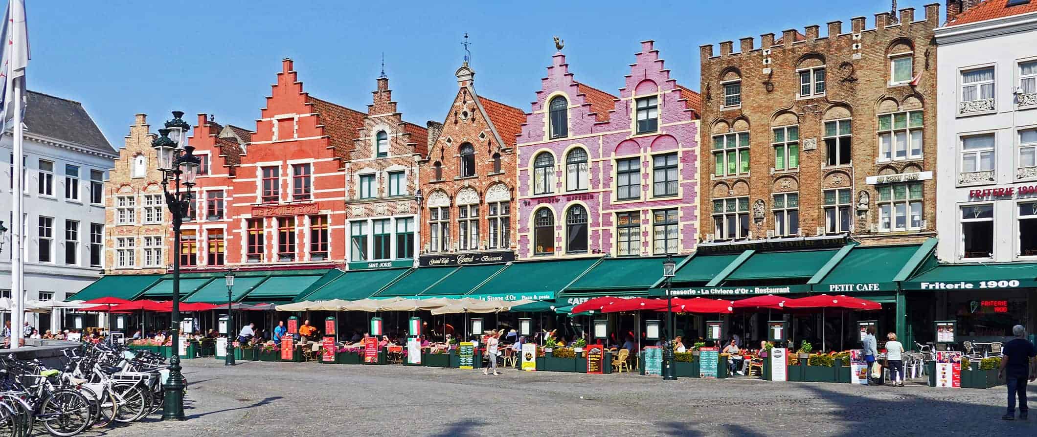 A colorful street of old row houses in Bruges, Belgium near a square full of people
