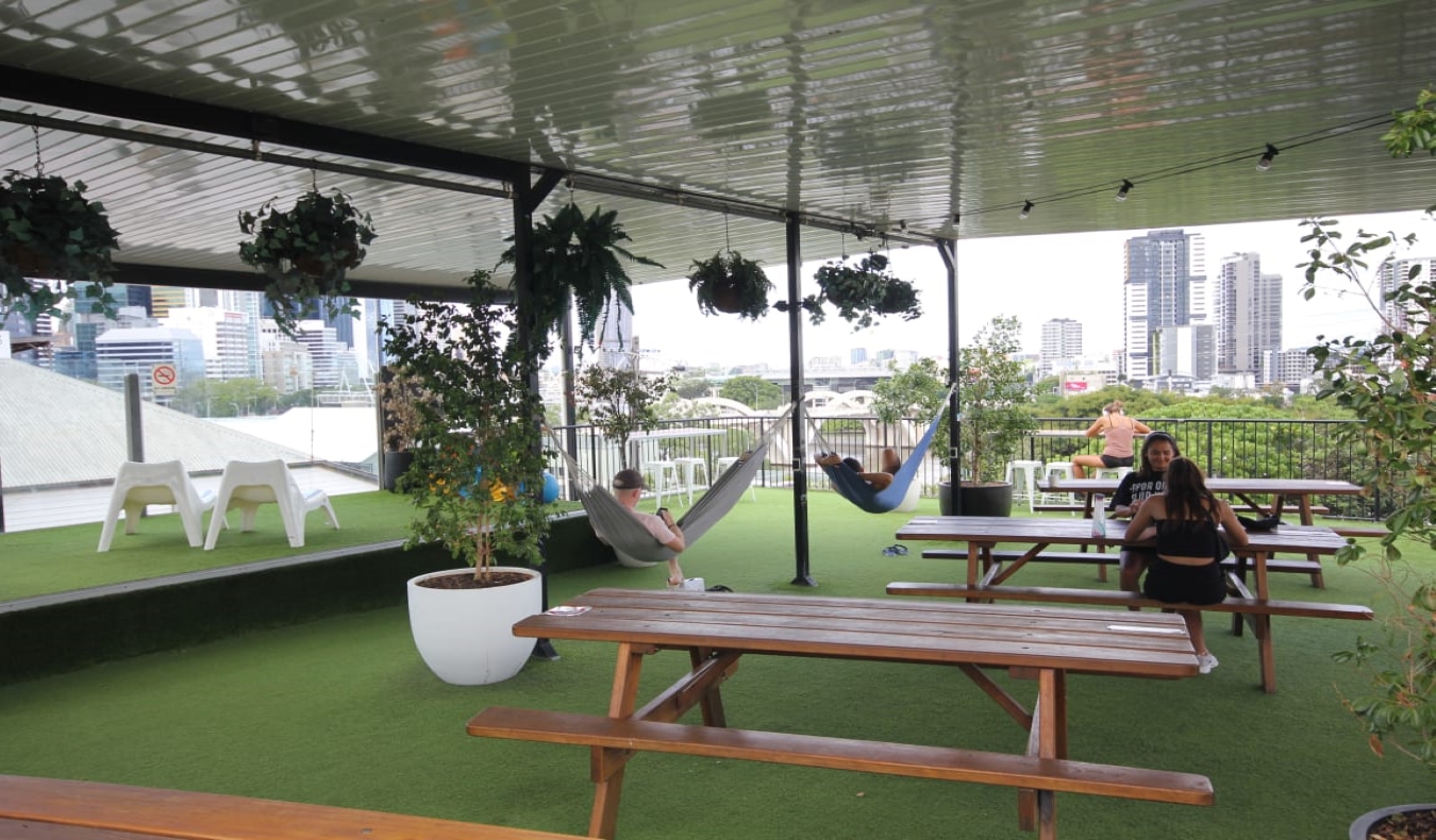 Rooftop terrace with picnic tables and people hanging out in hammocks at City Backpackers in Brisbane, Australia.