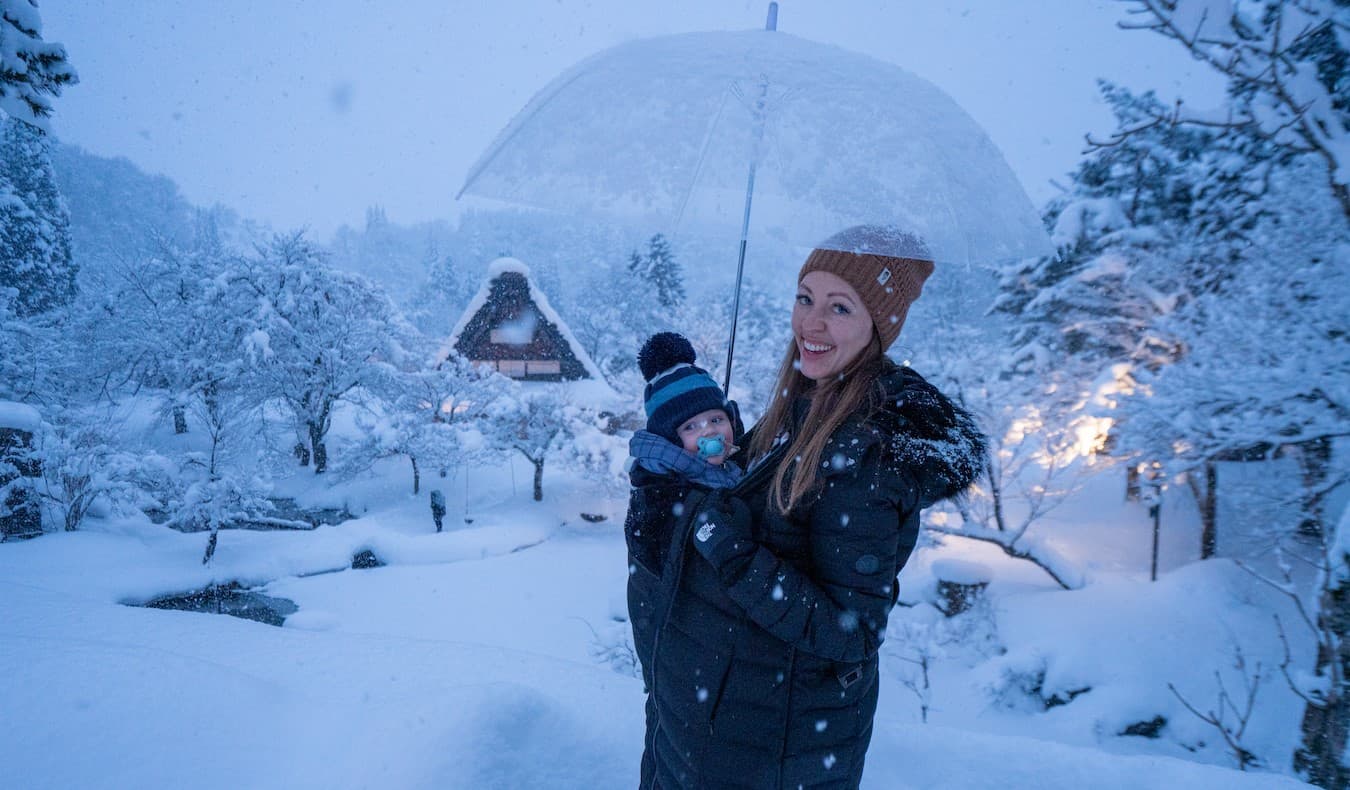 Blogger Kristin Addis of Be My Travel Muse with her infant son in a baby carrier as they stand in a snowy landscape in Japan