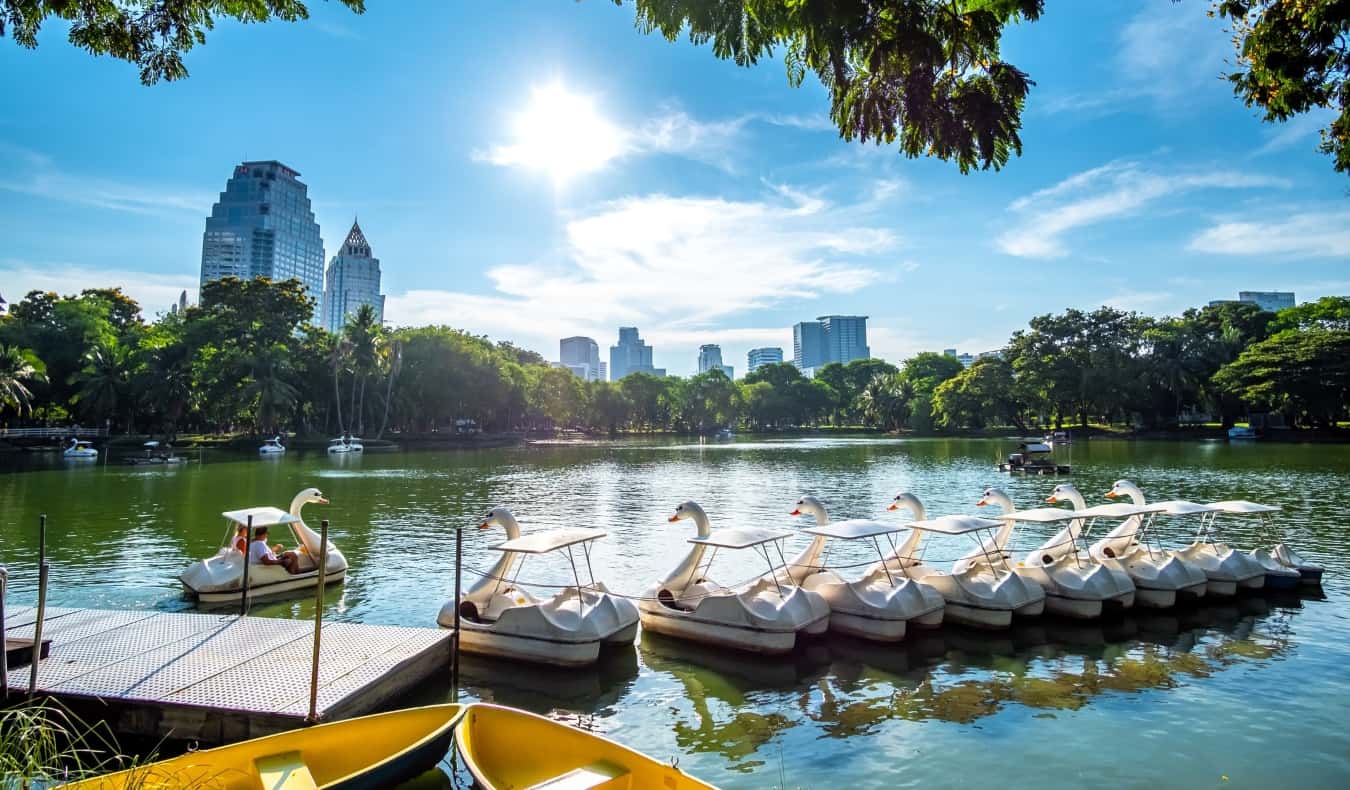 Swan boats on a lake with the city's skyscrapers in the background of Lumpini Park in Bangkok, Thailand