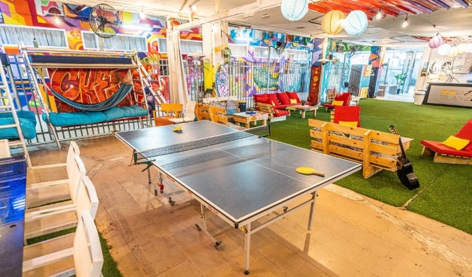 Bright and colorful common area with mural, hammocks, and ping pong table at Marina Ben-Gurion Hostel in Tel Aviv, Israel