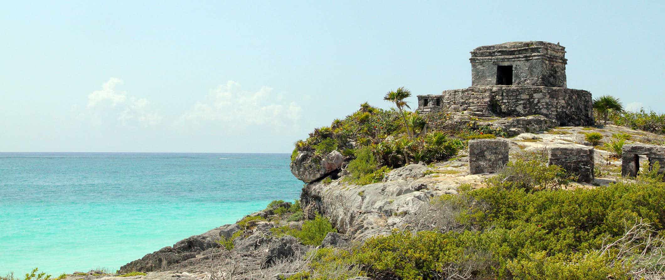 Historic ruins near the ocean in Tulum, Mexico with lush greenery on a sunny day