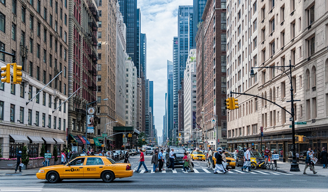 A busy intersection with a yellow cab in New York City with lots of people crossing the street