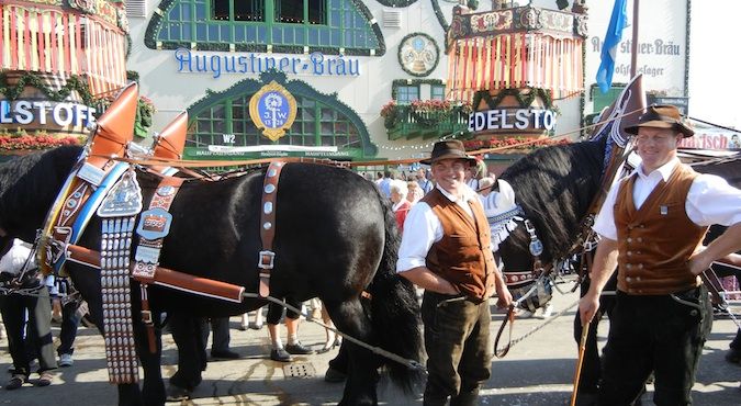 Men wearing traditional Bavarian outfits and standing my horses at Oktoberfest