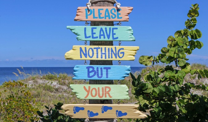 A sign near the beach that says leave nothing but footprints in different colors