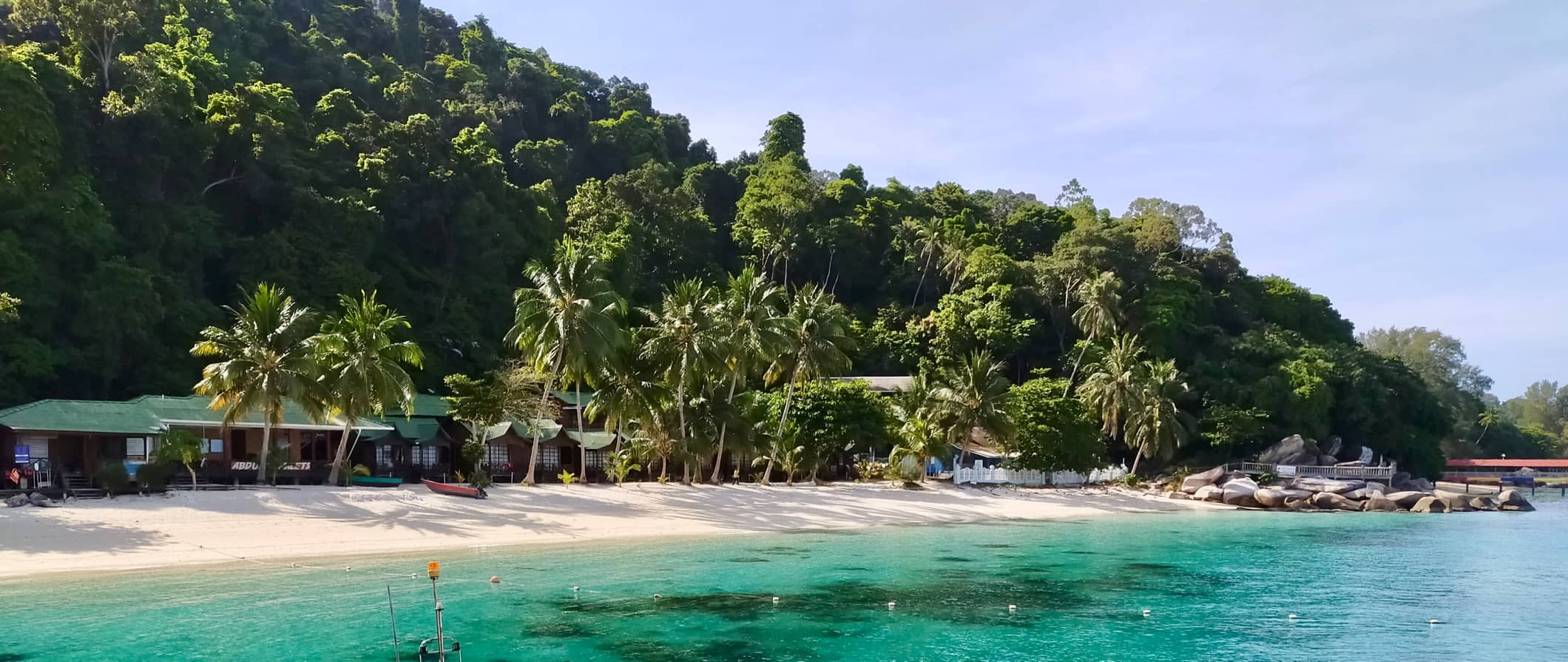 A stunning beach view in the Perhentian Islands, Malaysia with clear waters and lush palm trees and jungle