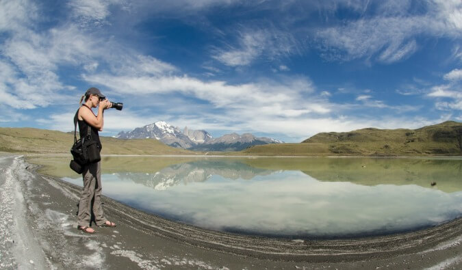 woman taking a photo with her DSLR camera of a mountain reflected in a lake